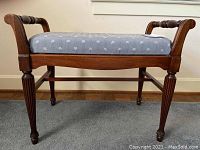 Side view of the wooden framed bench showing fluted legs and armrest details along with blue upholstered seat with small white leaf pattern.