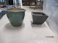 Two ceramic planters on floor, one round aqua and one rectangular gray
