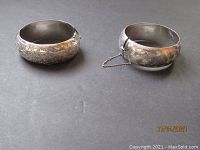 Two silver hinged cuff bracelets shown side by side, showing their overall size, shape, and embossed detailing