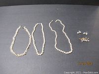 Overview of 3 necklaces, brooch, and earrings on gray background