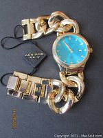 Gold tone women's wristwatch with turquoise blue dial and diamond hour markers, large chain link bracelet attached with Akribos XXIV hang tag.