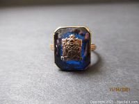 Close-up of the ring face showing the blue stone and gold crest emblem detail