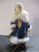Full frontal image of Byers' Choice Santa figurine in a blue coat holding a stick and greenery.
