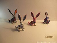 Four handcrafted whimsical rabbits with large ears and intricate painted floral designs in various colors, arranged on a plain background.