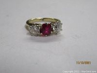 Front view of 14K gold ring showing central red ruby-like stone with one diamond on each side, one diamond chipped.