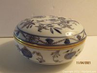 Side view of the closed porcelain covered trinket box featuring blue floral and gold trim designs.