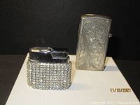 Both lighters side by side showing the glass-studded lighter and the silver case with floral engraving.