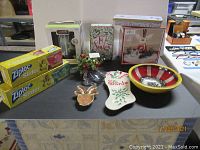 Overview photo showing all items included in the lot displayed on a table, including the hand-painted wooden bowl, ornaments, fragrance oil kit, LED candle, Lenox Santa figurine, tins, and Ziploc bags.