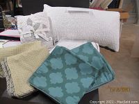 Photo showing various folded bedding items including patterned euro sham pillow covers and a white sheet set in plastic packaging.