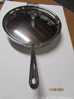Top view of large All-Clad sauté pan with lid placed upside down showing shiny finish and handle.
