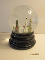 Front view showing London landmarks inside clear glass snow globe with black tiered wooden base.