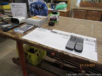 Photo showing part of the lot on a wooden table including manuals, remote controls, headphones, a case, small device, and white box.