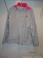 Front view of light grey The North Face women's jacket with pink hood lining, hung on hanger