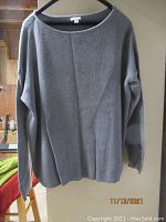 Taupe knit sweater with a textured diagonal and vertical ribbed pattern and boat neckline on hanger against wooden background.