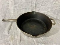 Griswold No. 90 frying pan bottom with nickel-plated handle and side helper handle shown in side profile on cloth.