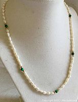 Front view of beaded necklace with white freshwater pearls and green turquoise stones on display bust