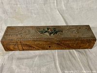 Top and side views of antique carved wooden pencil box showing detailed carved design and colored floral motif on lid