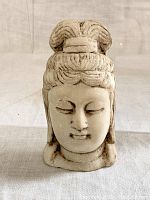 Front-facing view of stone-carved head showing hair bun, facial features, and base.