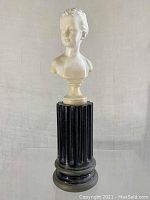 Front view of white bust of a girl on black fluted pedestal.