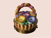 Front view of hand painted miniature flower basket pill box showing multi-colored flowers, twisted handle with pink ribbon detail and gold-tone metal base.