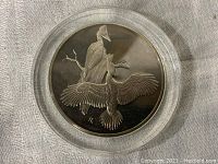 Obverse of coin showing two Pileated Woodpeckers sculpted in relief on silver surface.