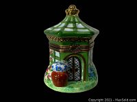 Front side view of the green and white hand painted gazebo pill box showing flower pot and door detail with metal clasp.