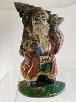 Front view of the heavy cast iron painted Santa Claus doorstop showing worn paint and detailed figure of Santa with tree on shoulder.