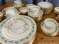 Photo showing arrangement of dinner plates, dessert plates, saucers, broth bowls, and teacups all with green leaf and gold trim pattern.
