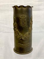 Front view of brass trench art vase showing embossed crest, figures and Verdun inscription.