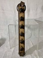 Front close-up of leather strap with seven metal sleigh bells spaced evenly along its length, showing patina on bells and well-stitched leather.