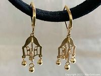 Close-up of pair of 14K gold dangly earrings showing detailed cut-out design and dangling gold balls.