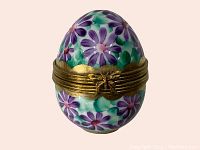 Front view of the hand-painted porcelain egg pill box showing purple daisies, green foliage, and gold metal band detail