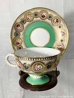 Front view showing teacup and saucer with floral and gold details, green color band, and twisted rope handle