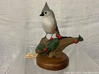 Front view of carved tufted titmouse perched on holly branch with round wood base