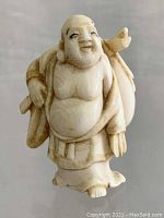 Front view of the carved Buddha figurine showing smile, robe details, and sack on the shoulder.