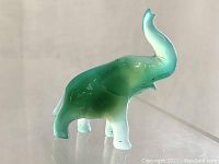 Side view of translucent green carved jade elephant figurine with stump raised, highlighting smooth polish and gradient color.