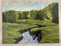 Front view of a small oil painting showing a winding creek surrounded by trees and grass under blue sky, signed by Claire Gagnon.