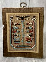 Front view of the Navajo sand painting with detailed sand art depicting symbolic figures and the Tree of Life motif, mounted on wood plaque with metal hanging handle.