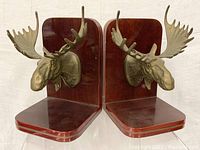 Front view of two brass moose head bookends with wood bases, showing detailed antlers and polished finish.