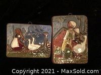 Two vintage ceramic tiles with raised relief rural scenes showing a girl with geese and a boy with a goose, taken in low light against black background.