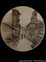 Front view of a round ceramic plate showing a detailed street scene with two people walking between buildings.