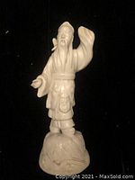 Front view of white porcelain Chinese man figurine with raised arm and detailed textured base.