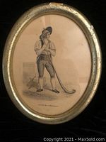 Front view of vintage oval picture depicting a man holding an alphorn, framed in wood with some damage and paint marks.
