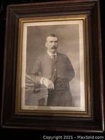 Front view of a framed vintage black and white photographic portrait of a man with a mustache wearing a striped suit and tie, in a dark wood frame with a gold trim.