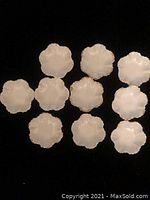 Eleven small white shell-shaped plates with scalloped and gold-trimmed edges arranged on a light background.