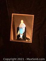 Front view of small rectangular vintage mirror picture frame showing image of woman holding a blue basket framed with gold-tone border.