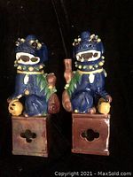 Front view of two blue porcelain dragon statues seated on square bases, showing detailed facial features, decorative collars, and spheres held by dragons. Left dragon has visible damage on right side.