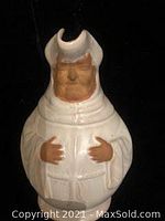 Front view of vintage porcelain pot shaped as a man with hat and robe, showing detailed face and hands