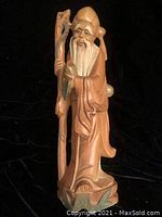 Front view of the wooden figurine showing facial details, beard, staff, and robe with cracks visible