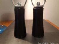Pair of black Peugeot salt and pepper mills showing front view with metal handles and matte black bodies.